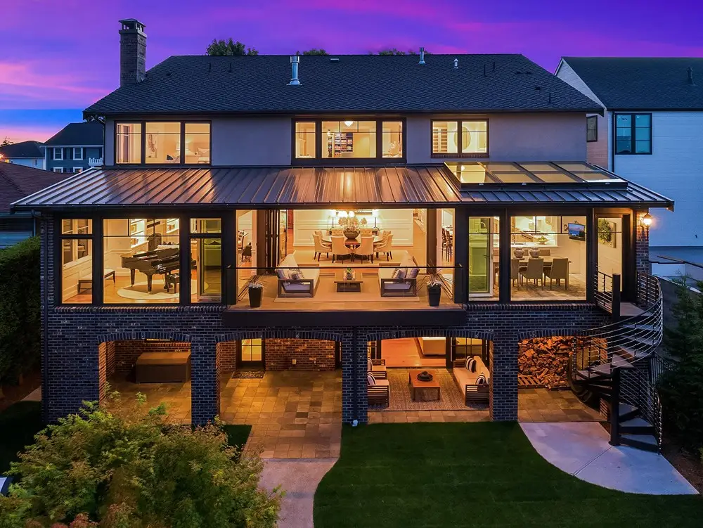 Rear elevation of the Magnolia residence illuminated at dusk with expansive glazing and multiple outdoor living levels.