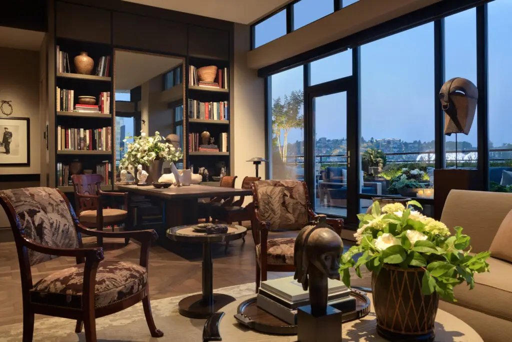 Open-concept living room with custom shelving, seating area, and panoramic city views through expansive windows.